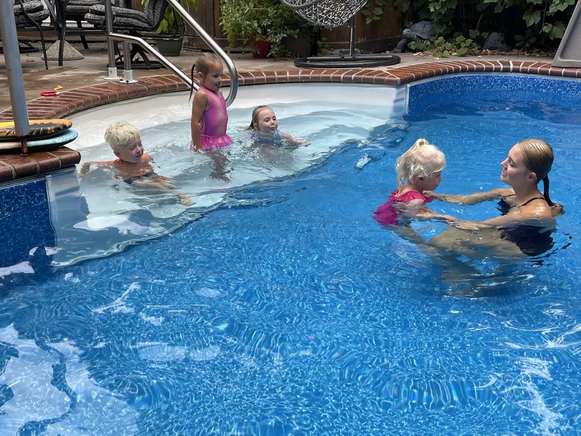 Tayelyn working with a small swimmer in the deeper water while three other children wait on the pool steps