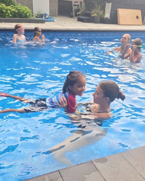 Annika supporting a grinning child on their front while Tayelyn works with another swimmer behind them