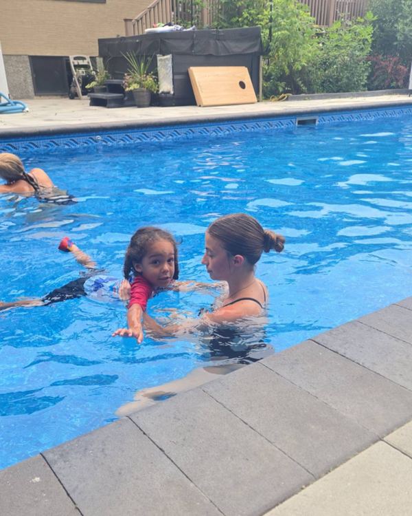 Annika guiding a child to reach forward and stretch out, with Tayelyn teaching further down the pool